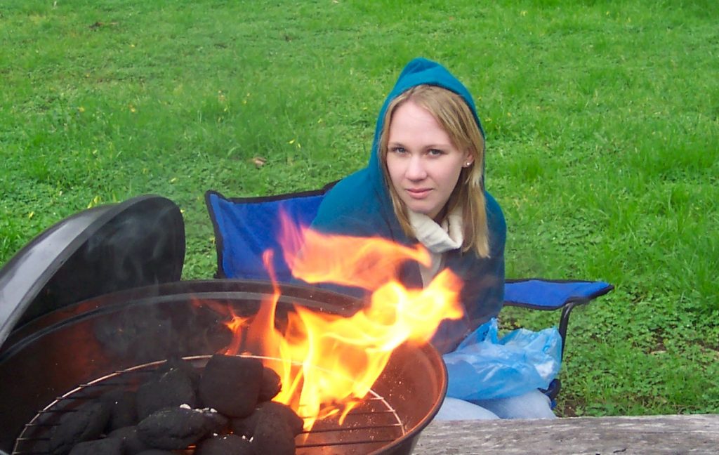 Blonde girl looking at you over flame from bbq